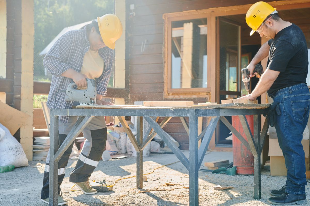 Two workers in hard hats cut and drill lumber on a jobsite, a common source of dropped tool close calls