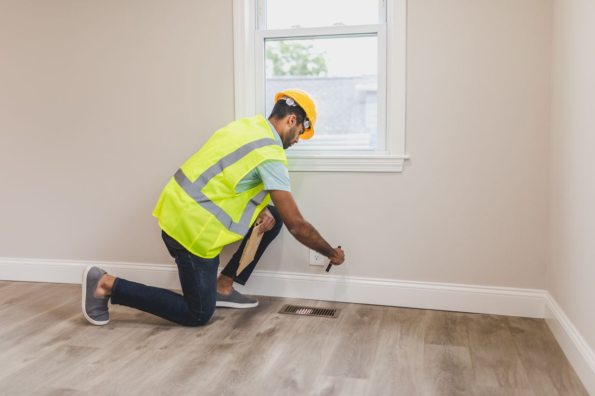 A safety professional in a hard hat inspects an electrical outlet during a site walkthrough
