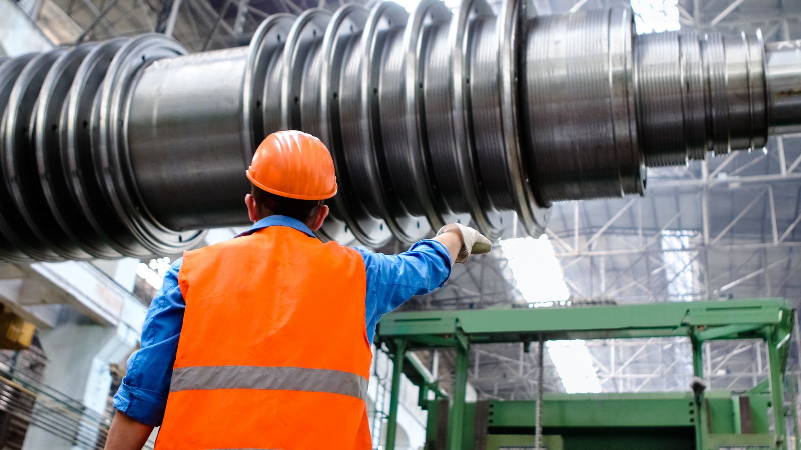 Safety worker in a hi-vis vest and hard hat inspecting large industrial machinery in a manufacturing plant