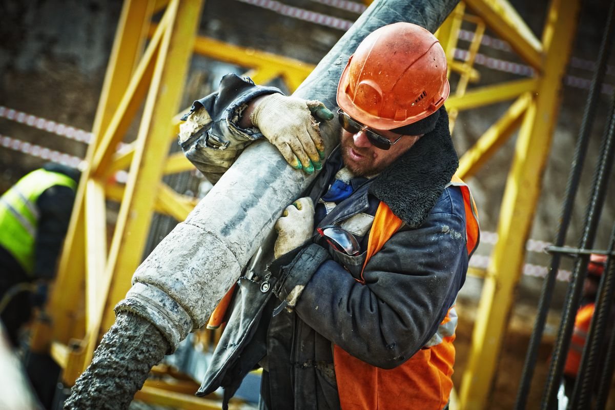 Construction worker in hard hat and full PPE guiding a concrete pump line on a jobsite